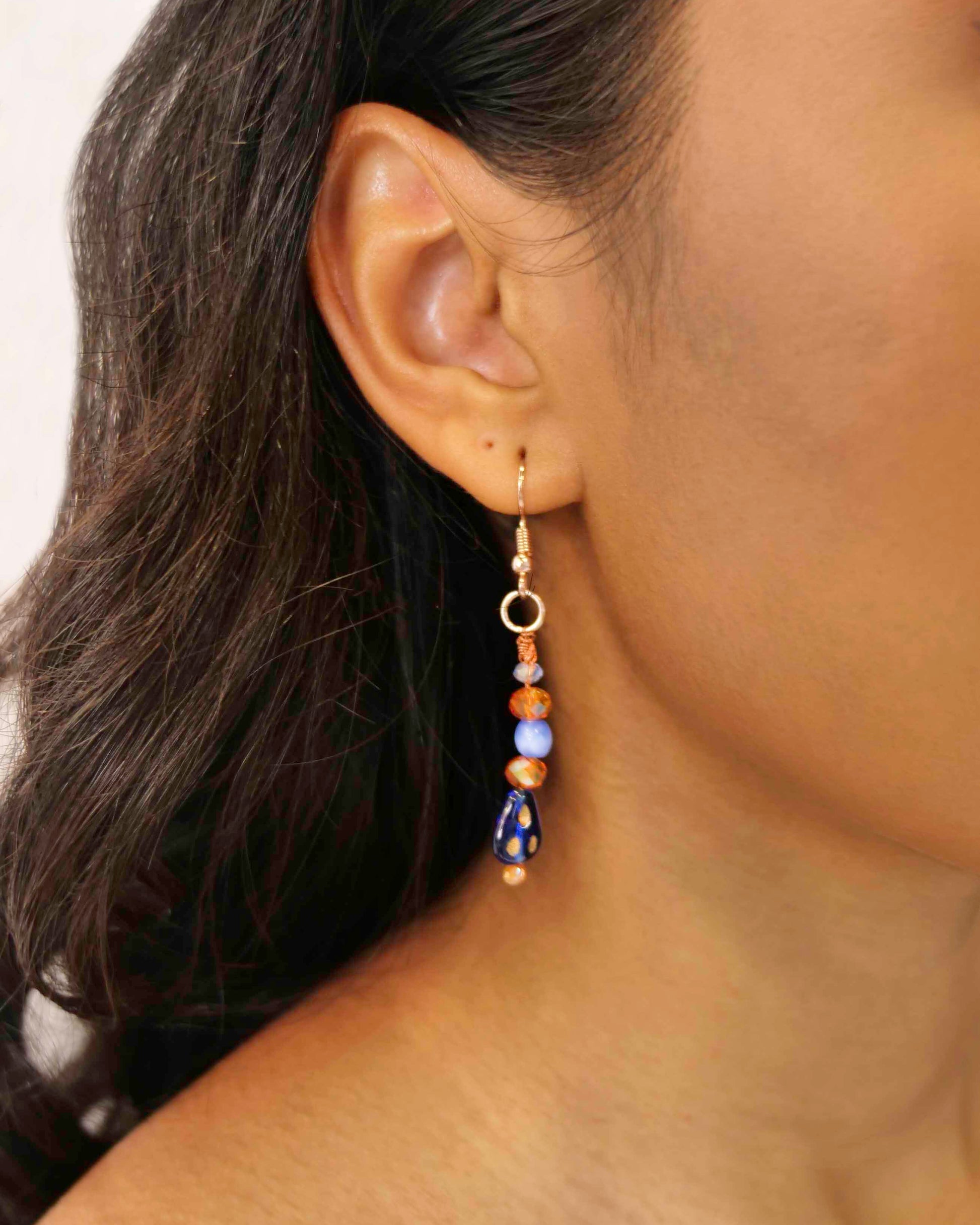 A handmade orange and blue crystal beaded pair of dangle drop earrings with blue glass charms.