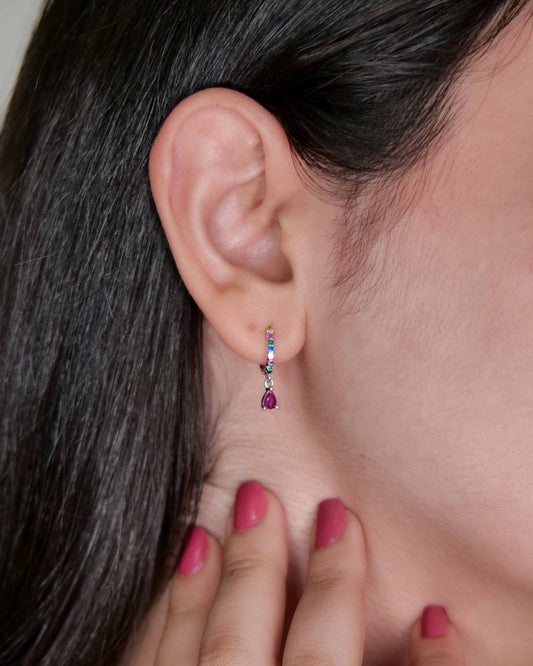 Close-up of an ear with a diamond earring and hand adjusting it, against a neutral background.