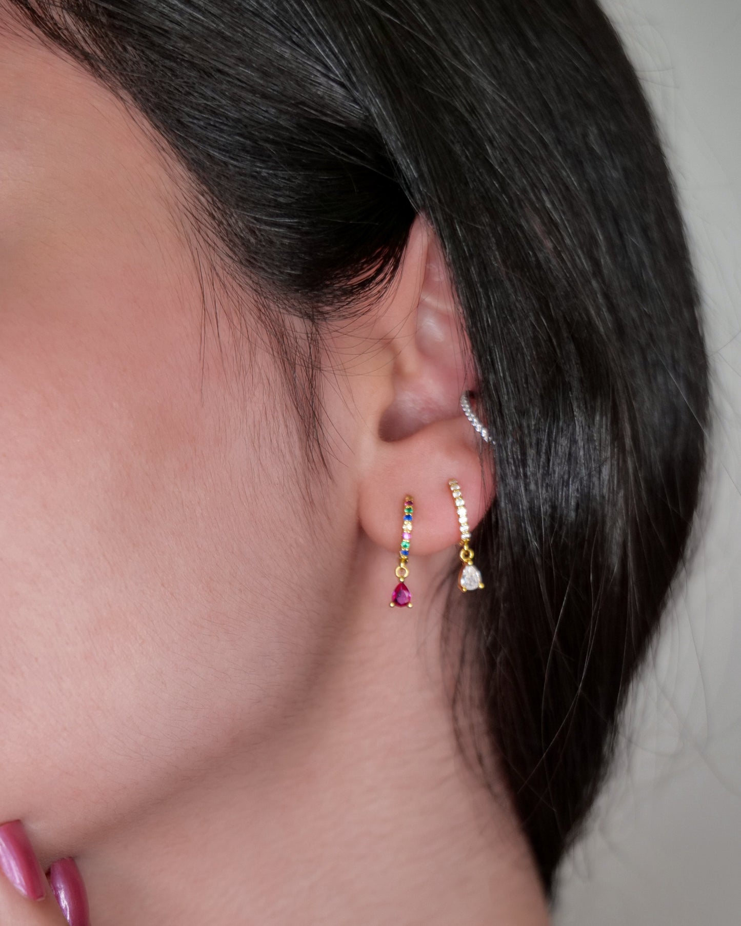 Close-up of a person wearing gold earrings with gemstones.