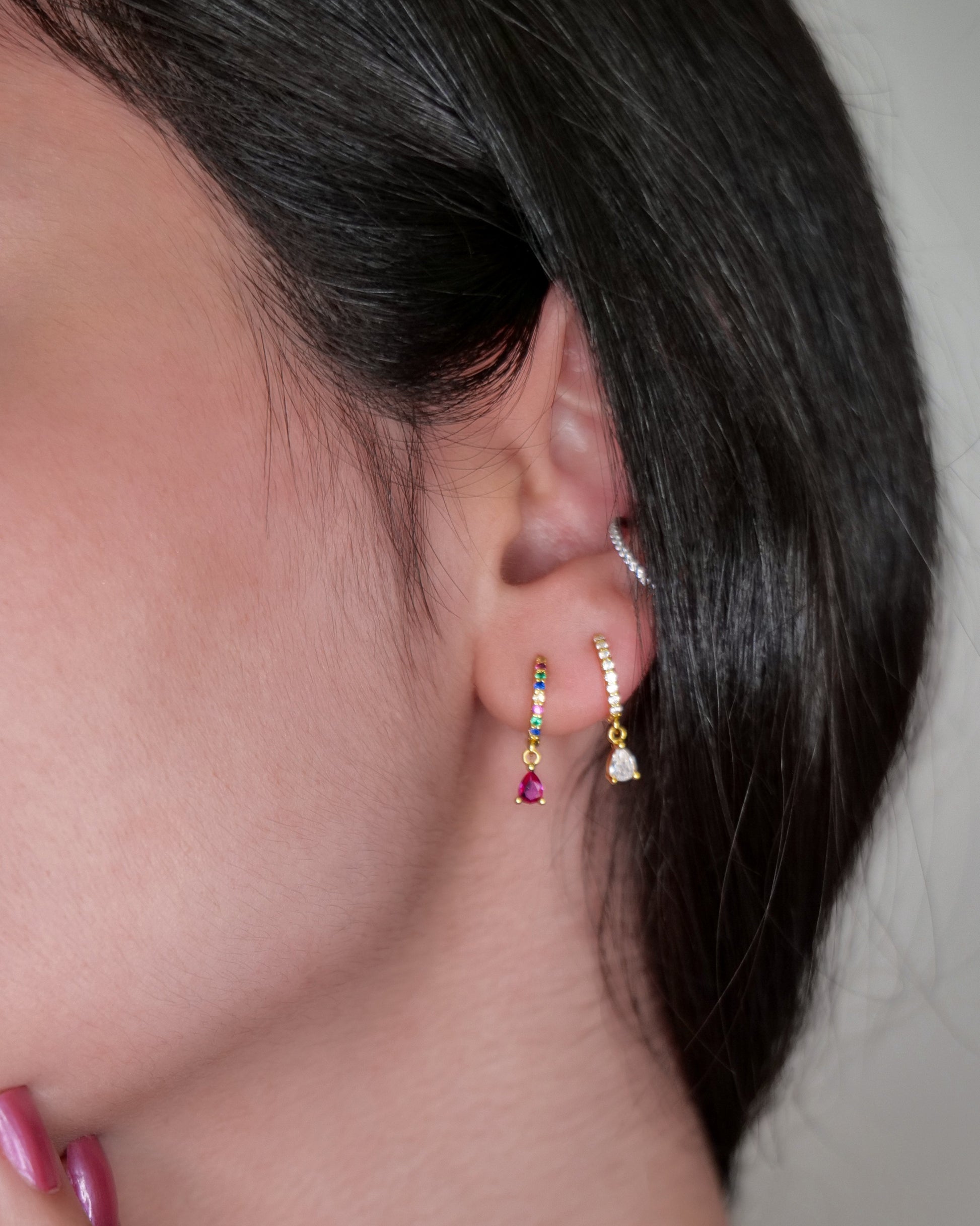Close-up of a person wearing gold earrings with gemstones.