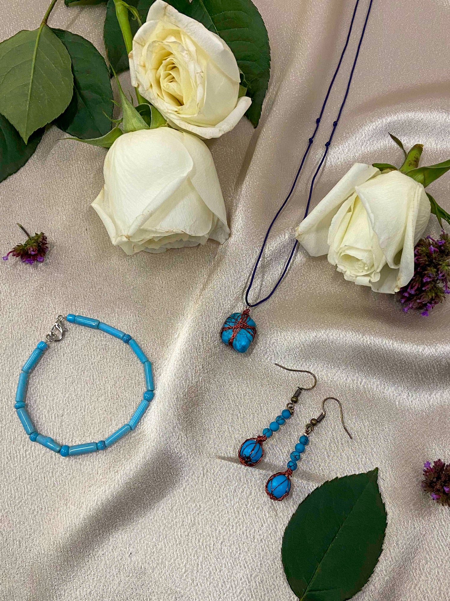 A pair of handcrafted wire-wrapped and beaded turquoise earrings, a matching pendant necklace, and beaded bracelet.