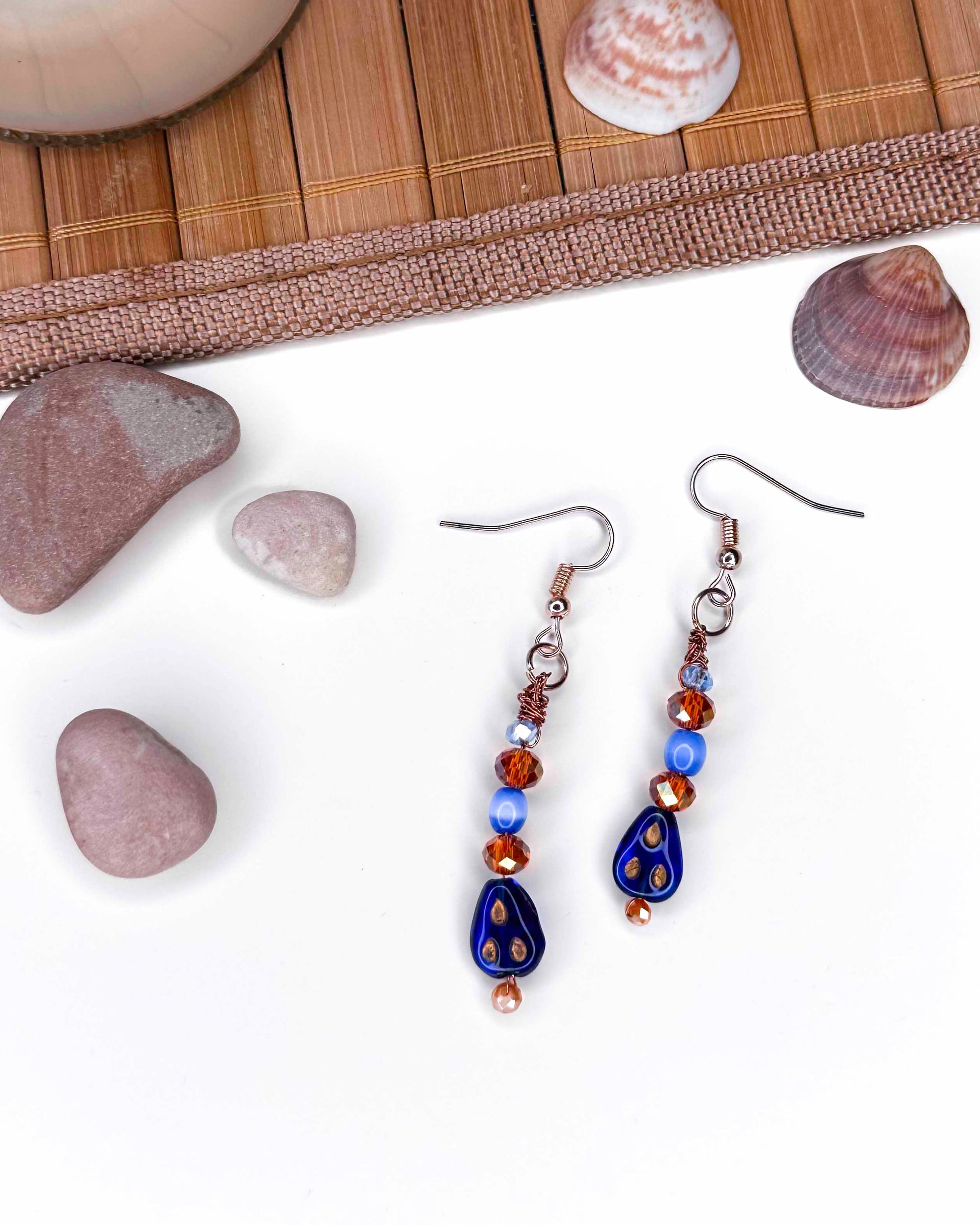 A handmade orange and blue crystal beaded pair of dangle drop earrings with blue glass charms.