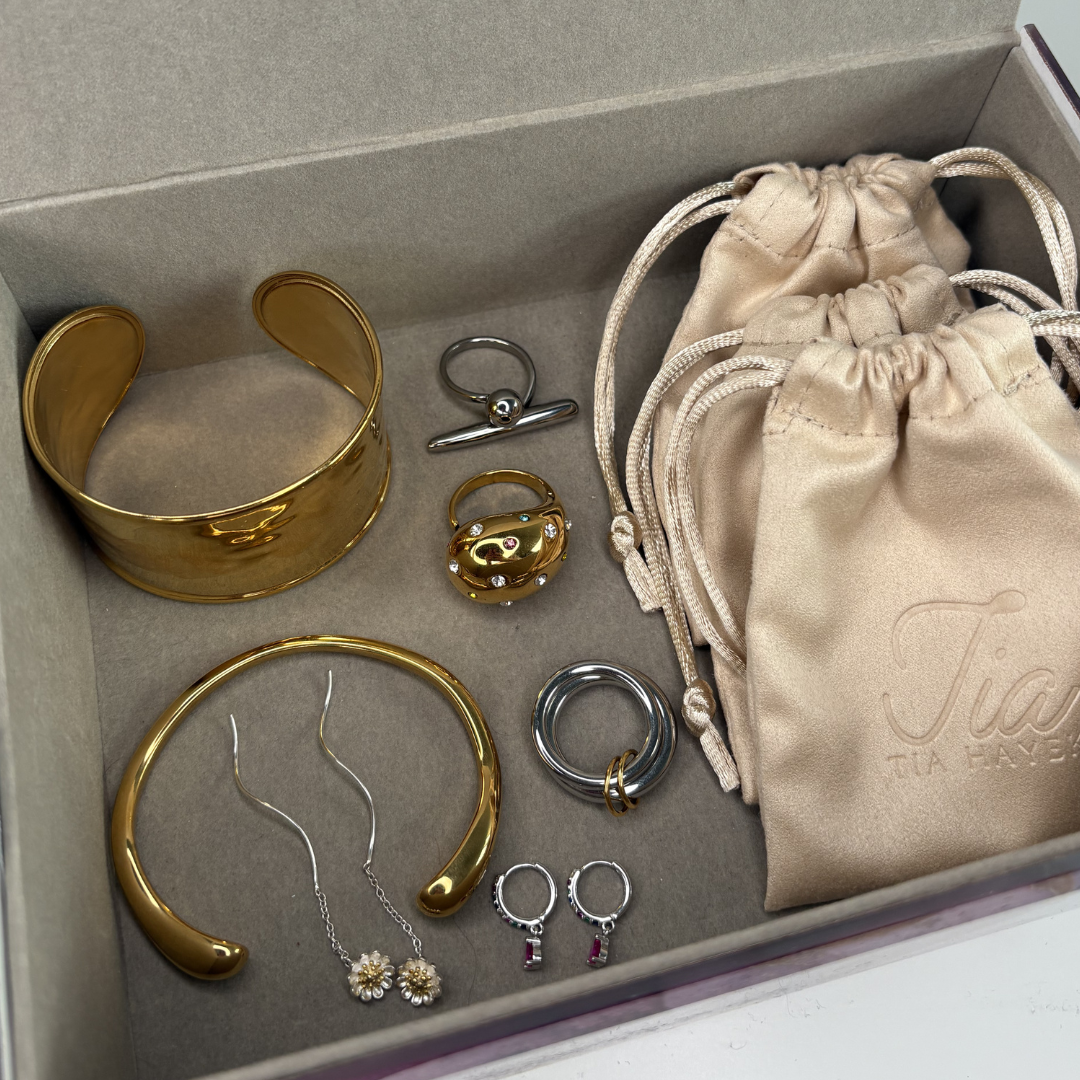 A lined jewelry box with stainless gold plated bangles, rings and earrings. Sterling silver and stainless steel rings and earrings.