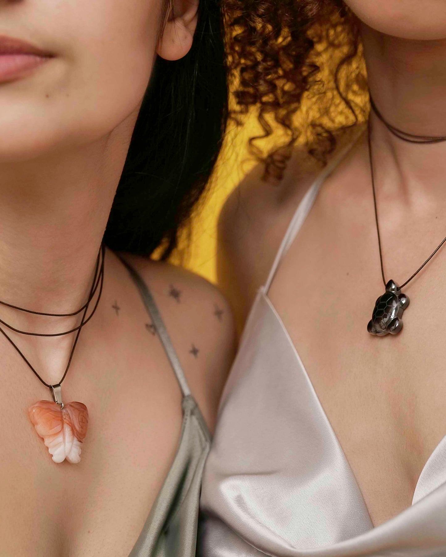 Handmade orange agate butterfly pendant necklace with a black vegan leather string, and a hematite turtle pendant necklace with brown leather string.
