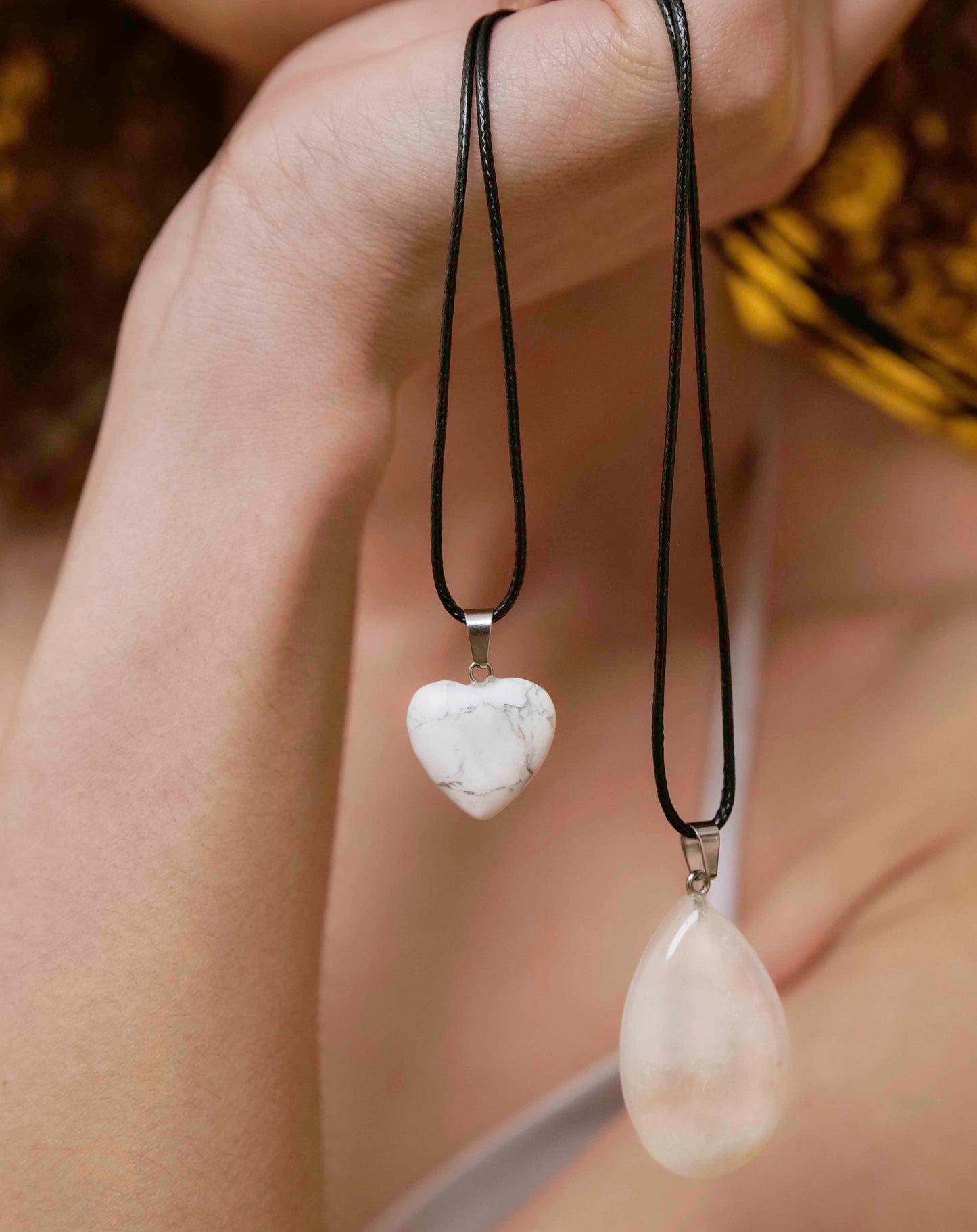 A handmade howlite heart pendant necklace with a black vegan leather string, and A handmade white jade teardrop pendant necklace with a black vegan leather string.