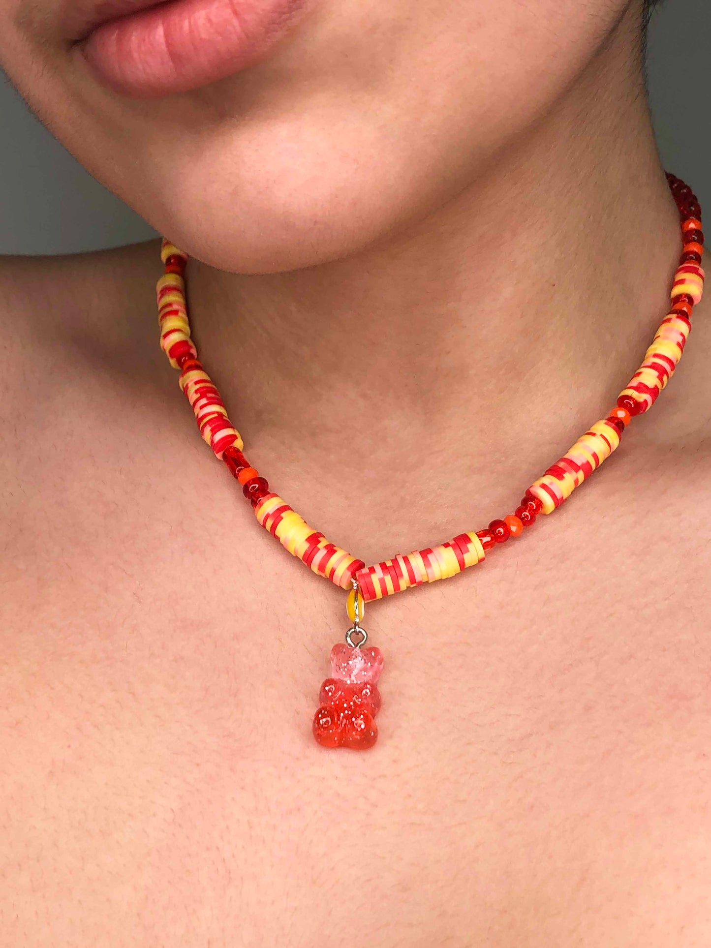 handcrafted necklace beaded using red, orange, yellow and pink glass and flat rubber beads. Accompanied by a yellow evil eye, and pink and orange gummy bear-like charm.