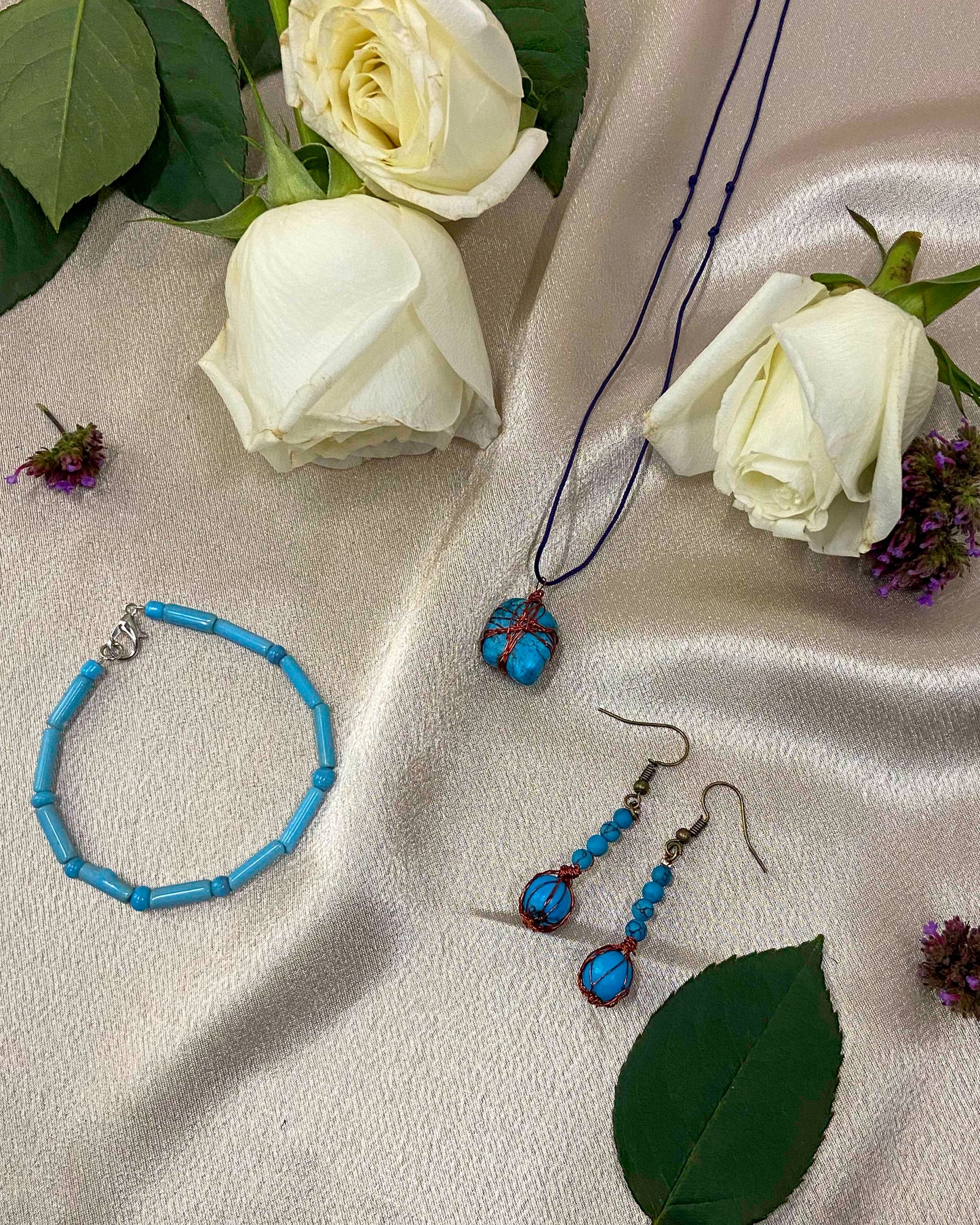 A pair of handcrafted wire-wrapped and beaded turquoise earrings, a matching pendant necklace, and beaded bracelet.