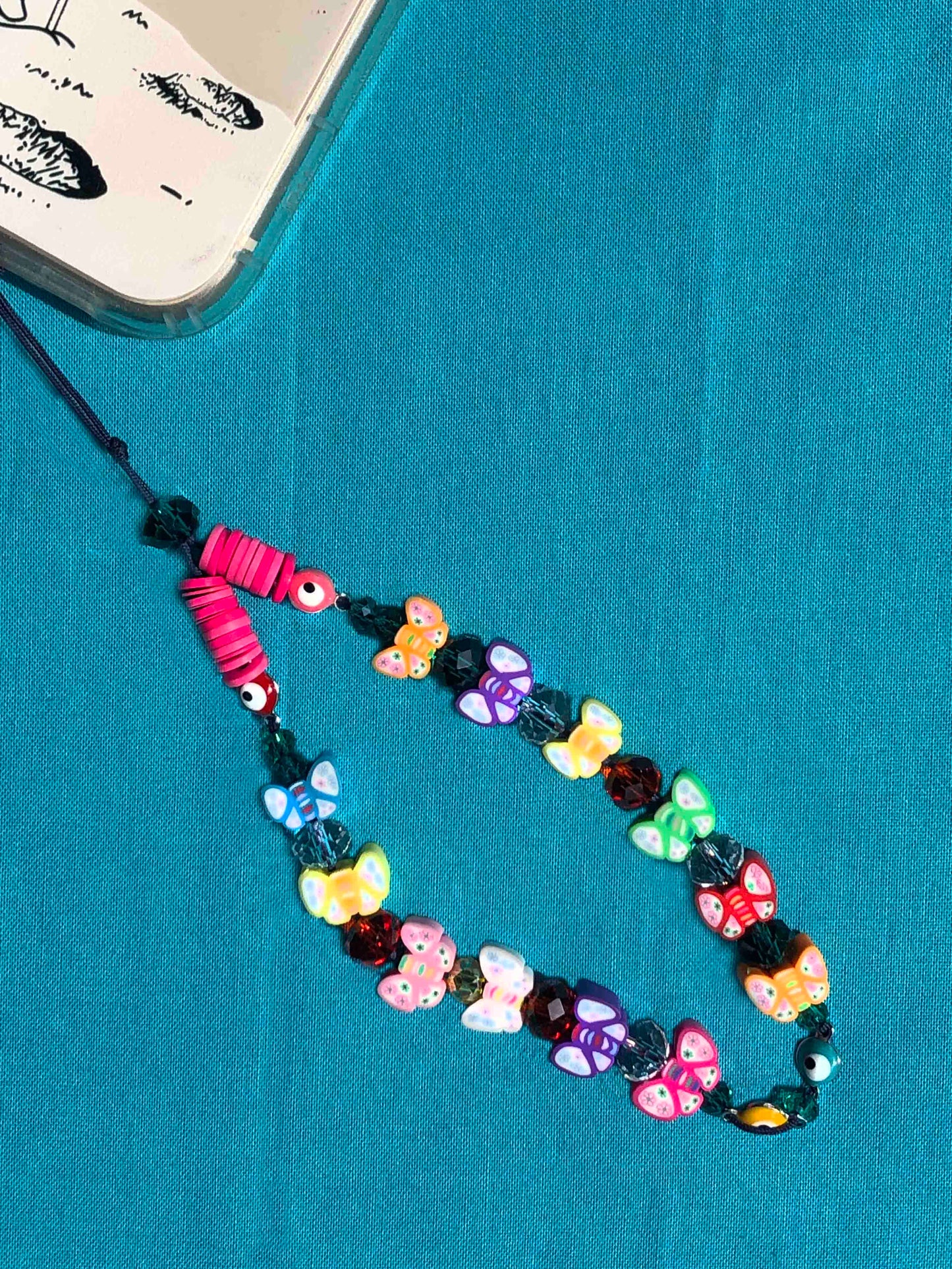 handcrafted multicolored beaded phone wrist strap made using butterfly charms, crystal and flat rubber beads, and four evil eye charms.