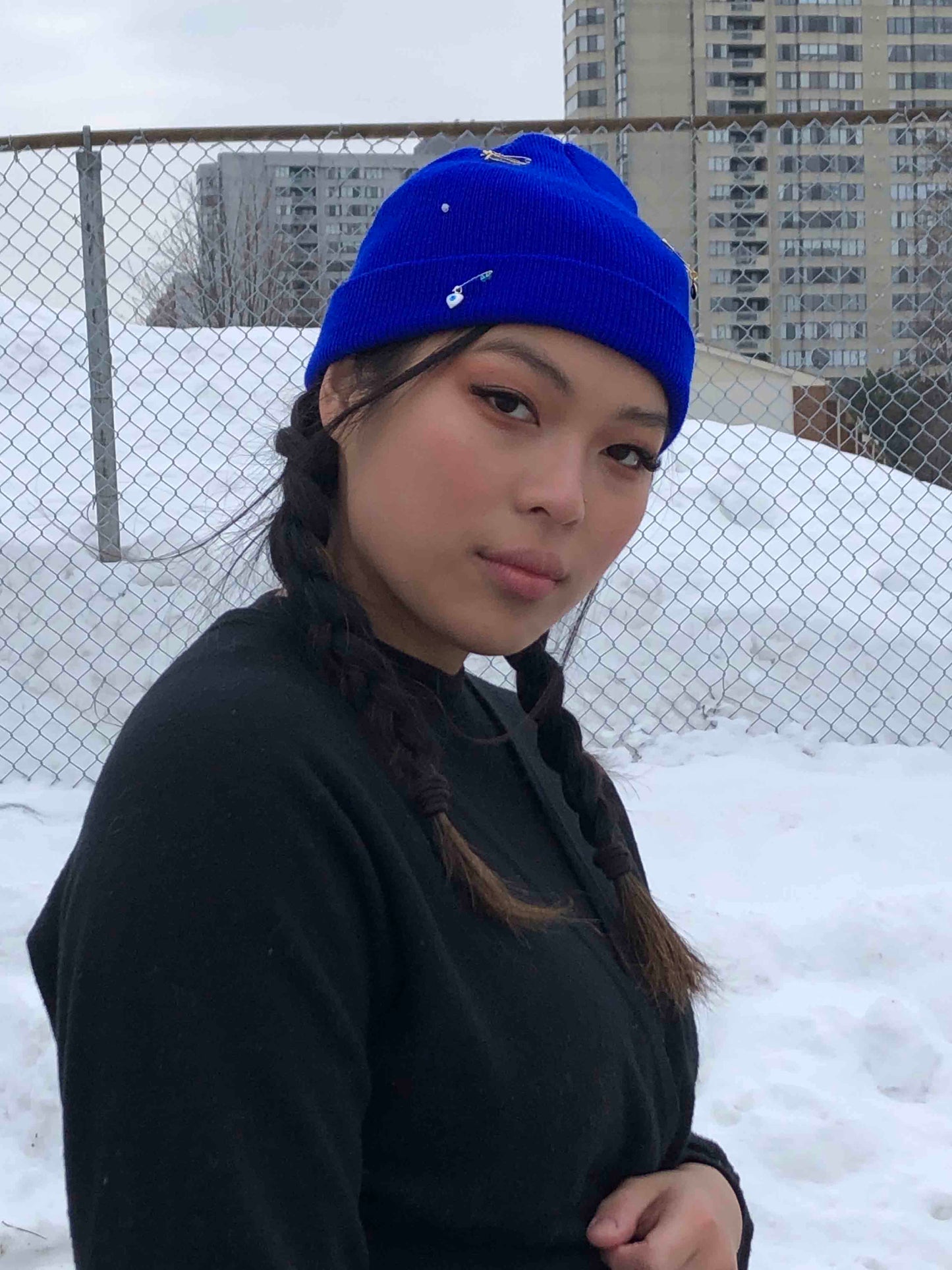 A blue wool knit beanie decorated with safety pins, evil eye charms and crystal beads.