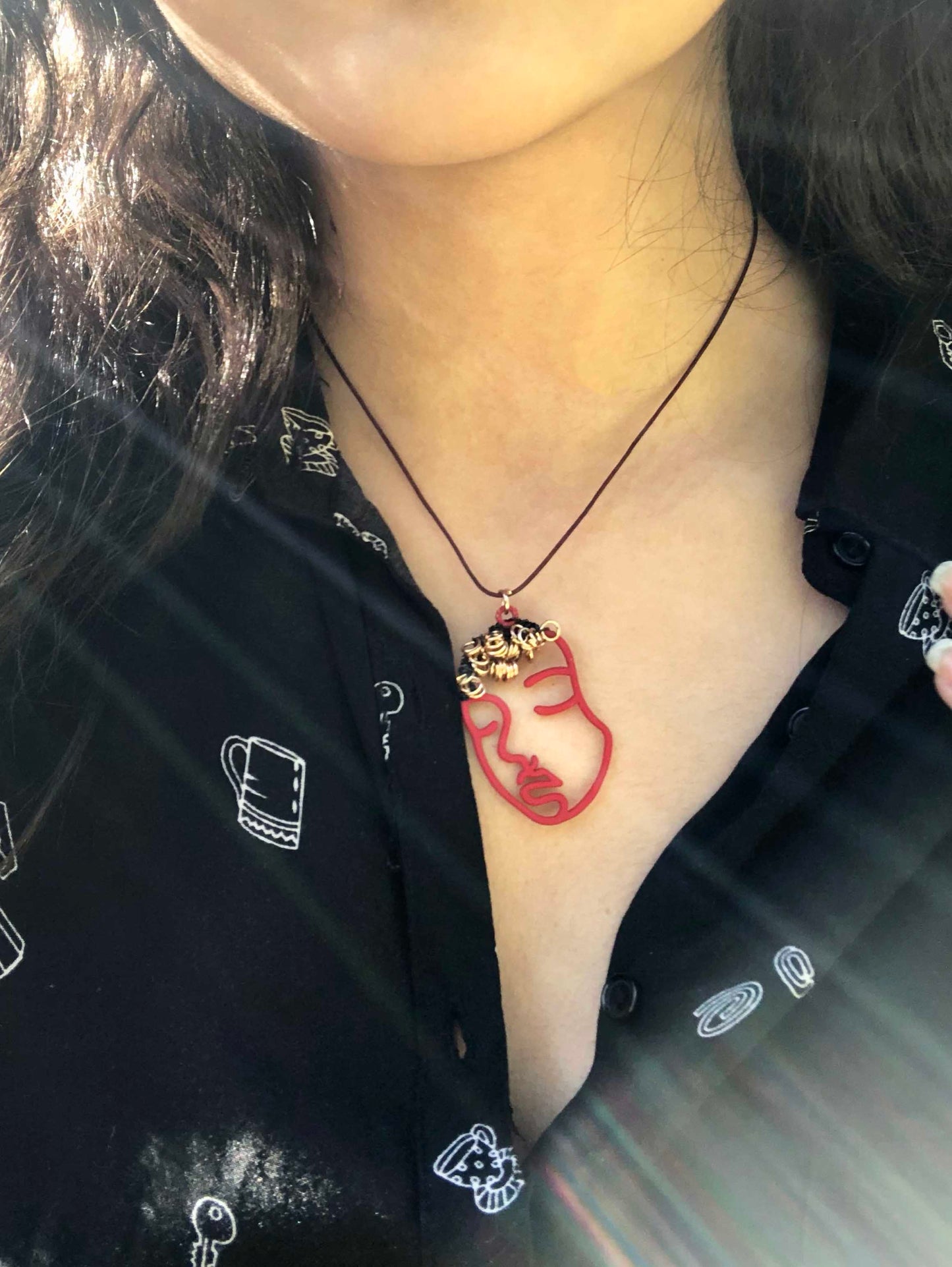 Pendant necklace made using a red hollowed-out face charm wire wrapped & beaded with small golden rings.
