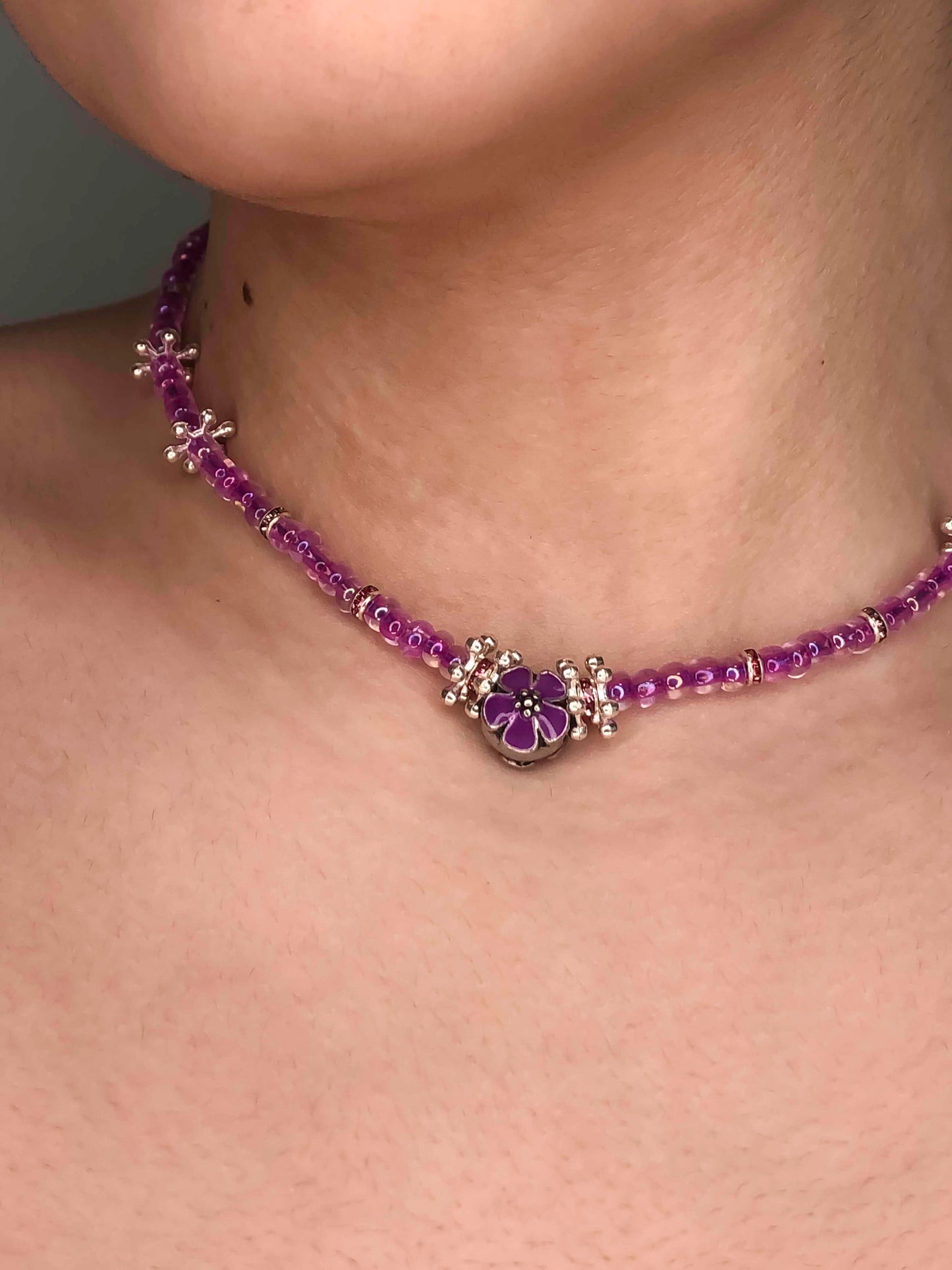 Handmade glass beaded necklace with silver flower charms, and a purple flower charm centerpiece.