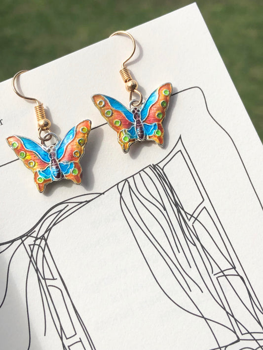A dangling pair of blue, orange & green butterfly charm earrings.