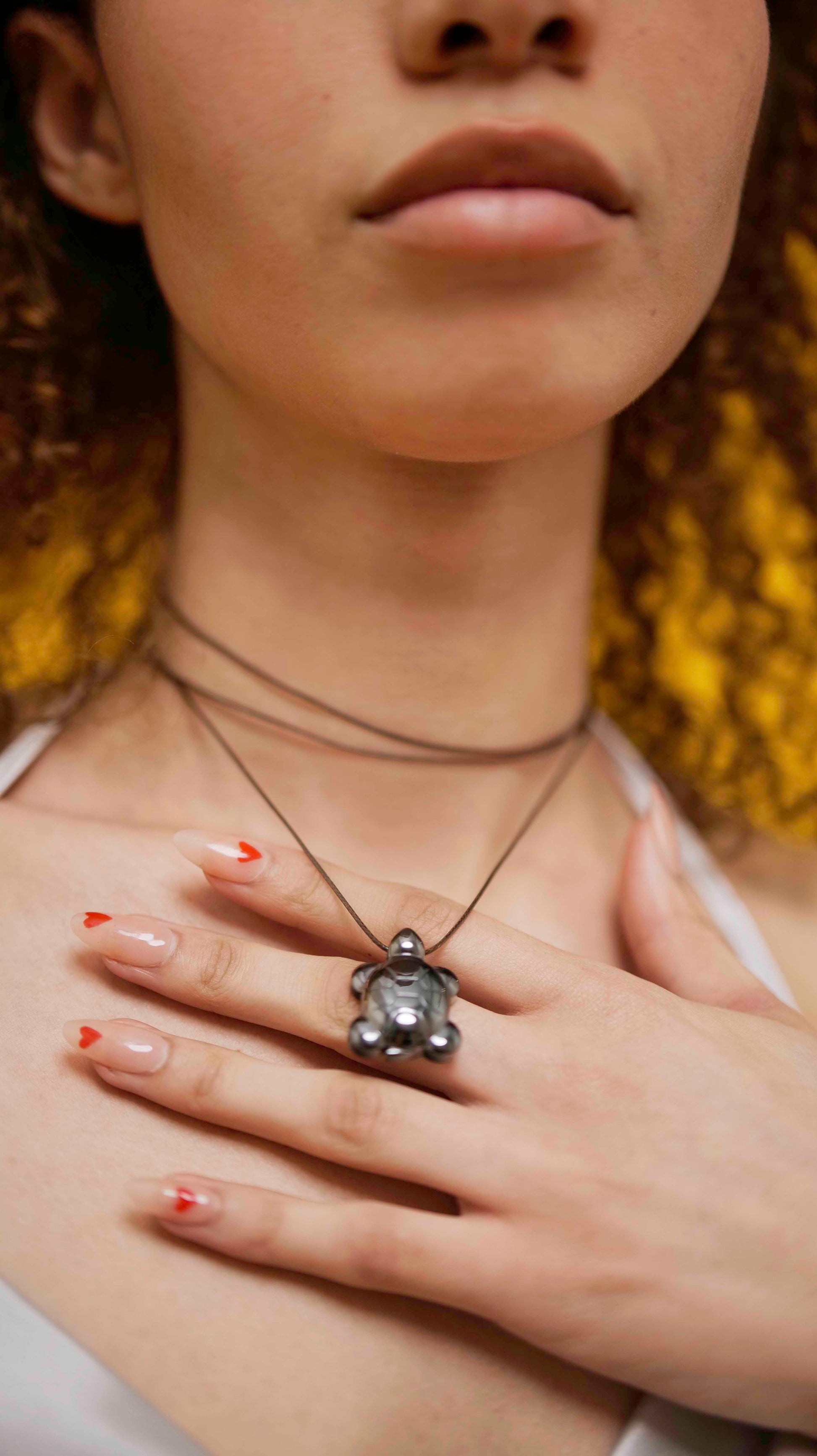 A handmade hematite turtle pendant necklace with brown leather string.