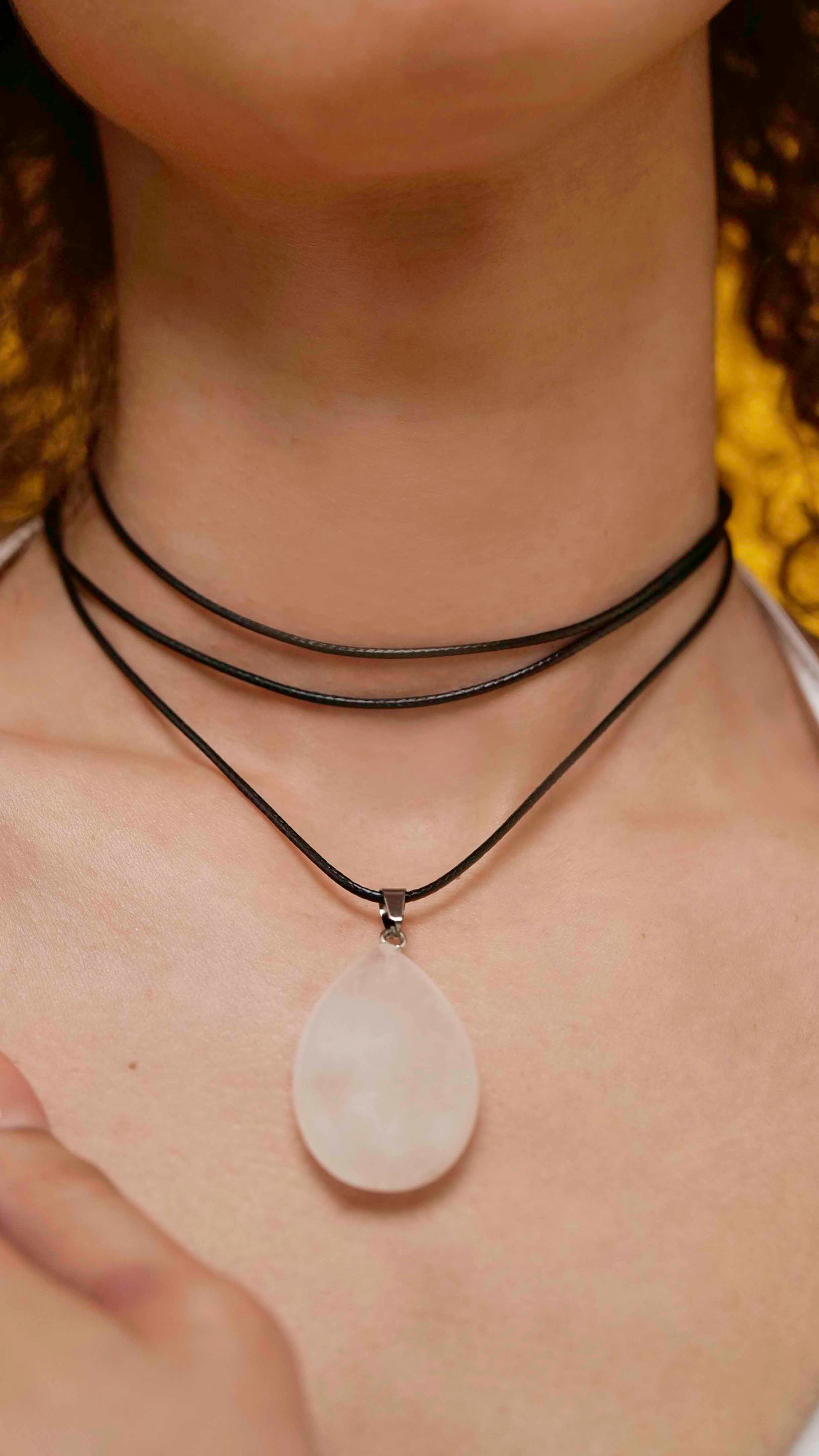 A handmade white jade teardrop pendant necklace with a black vegan leather string.