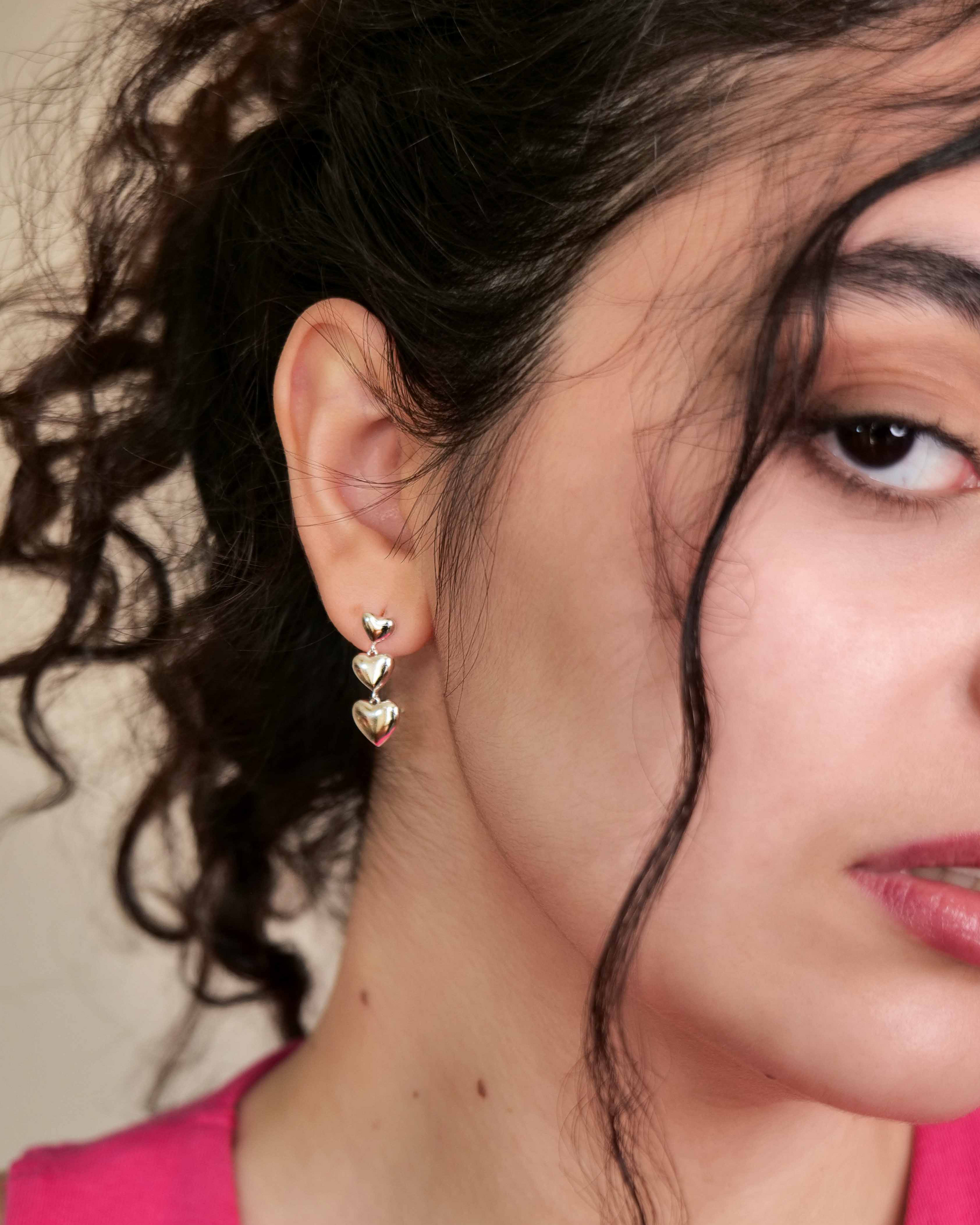 Close-up of a person wearing heart-shaped dangle drop earrings. 925 sterling silver earrings.