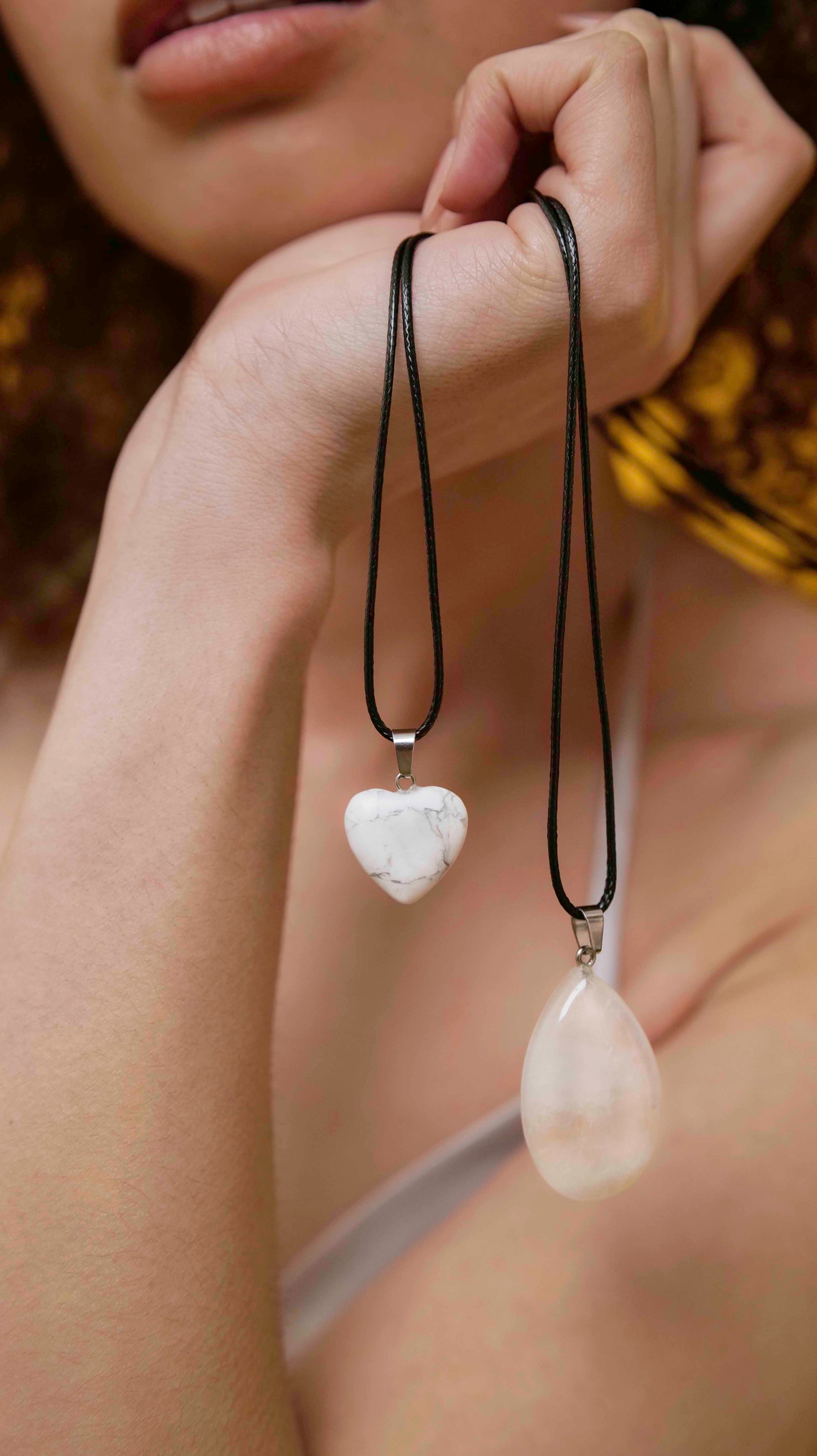 A handmade white jade teardrop pendant necklace with a black vegan leather string, and a howlite heart pendant necklace with a black vegan leather string.