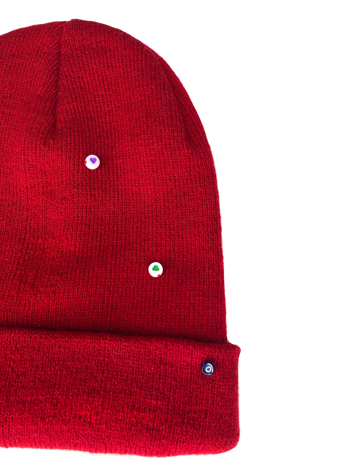 A red wool knit beanie decorated with both multicolor circle heart beads, and an evil eye charm.