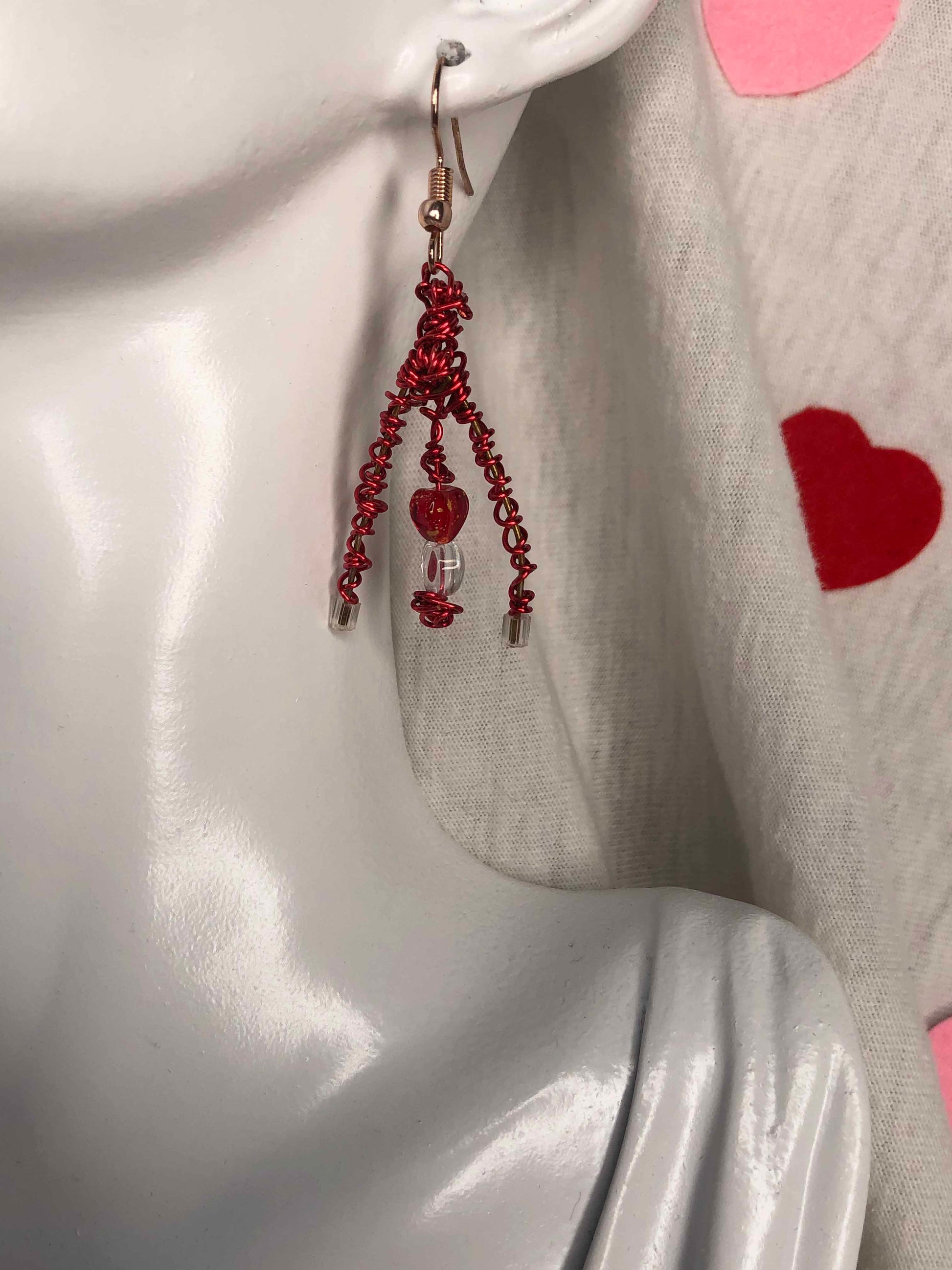 A pair of mismatched asymmetrical earrings wire wrapped using red and gold wires with clear & red heart beads, and a red crystal bead.