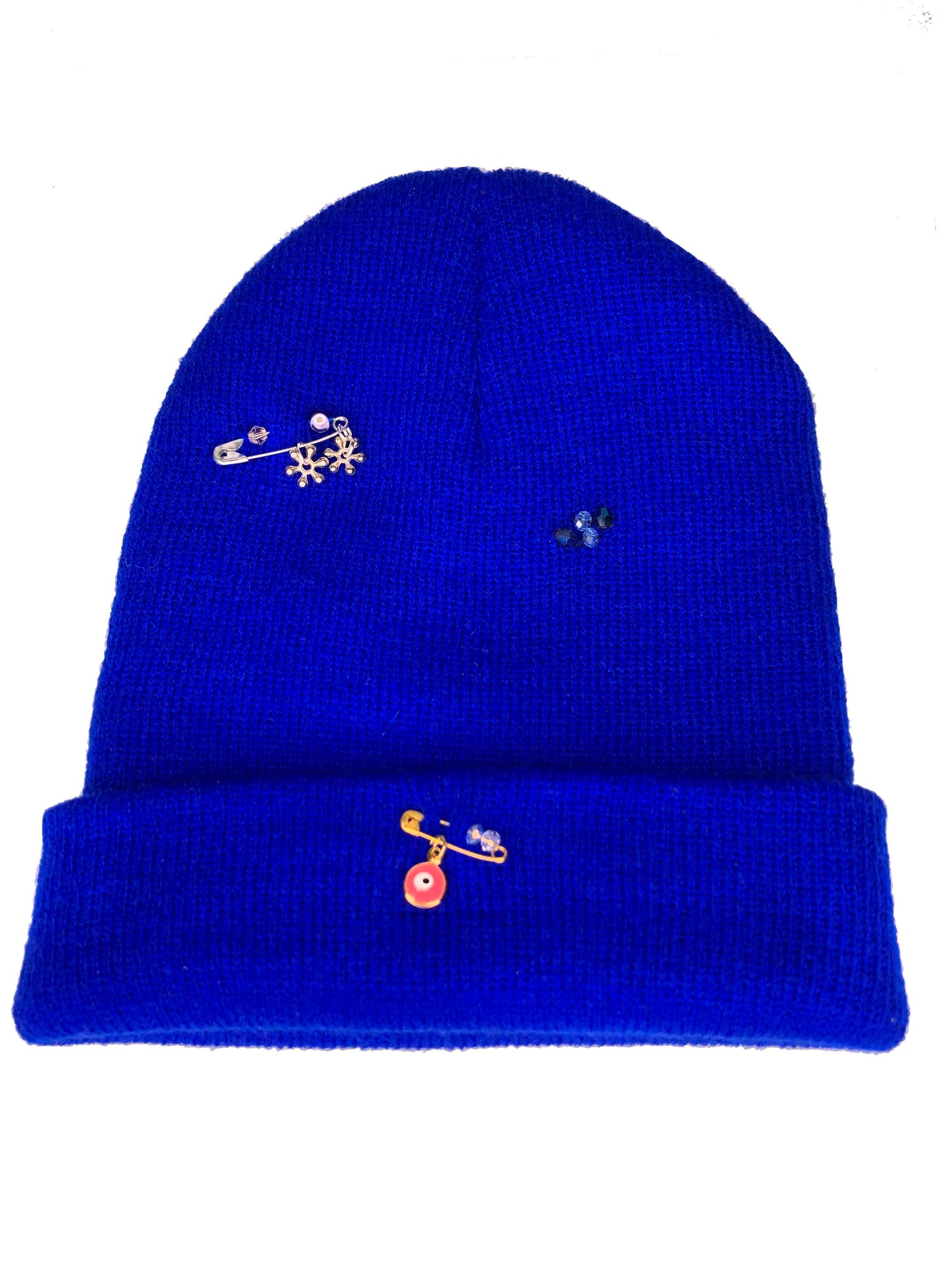A blue wool knit beanie decorated with safety pins, flower and evil eye charms, and crystal beads.