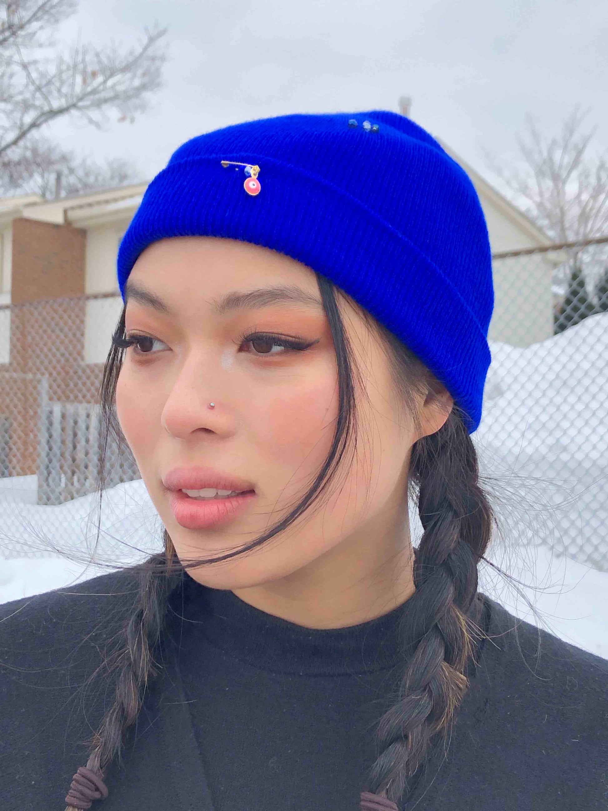 A blue wool knit beanie decorated with safety pins, evil eye charms and crystal beads.