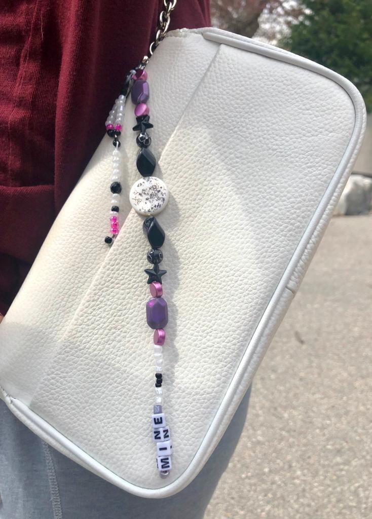 White, black, purple and pink beaded bag charm. Handcrafted with black stars, a coin floral print charm, and mine beaded using letter beads.
