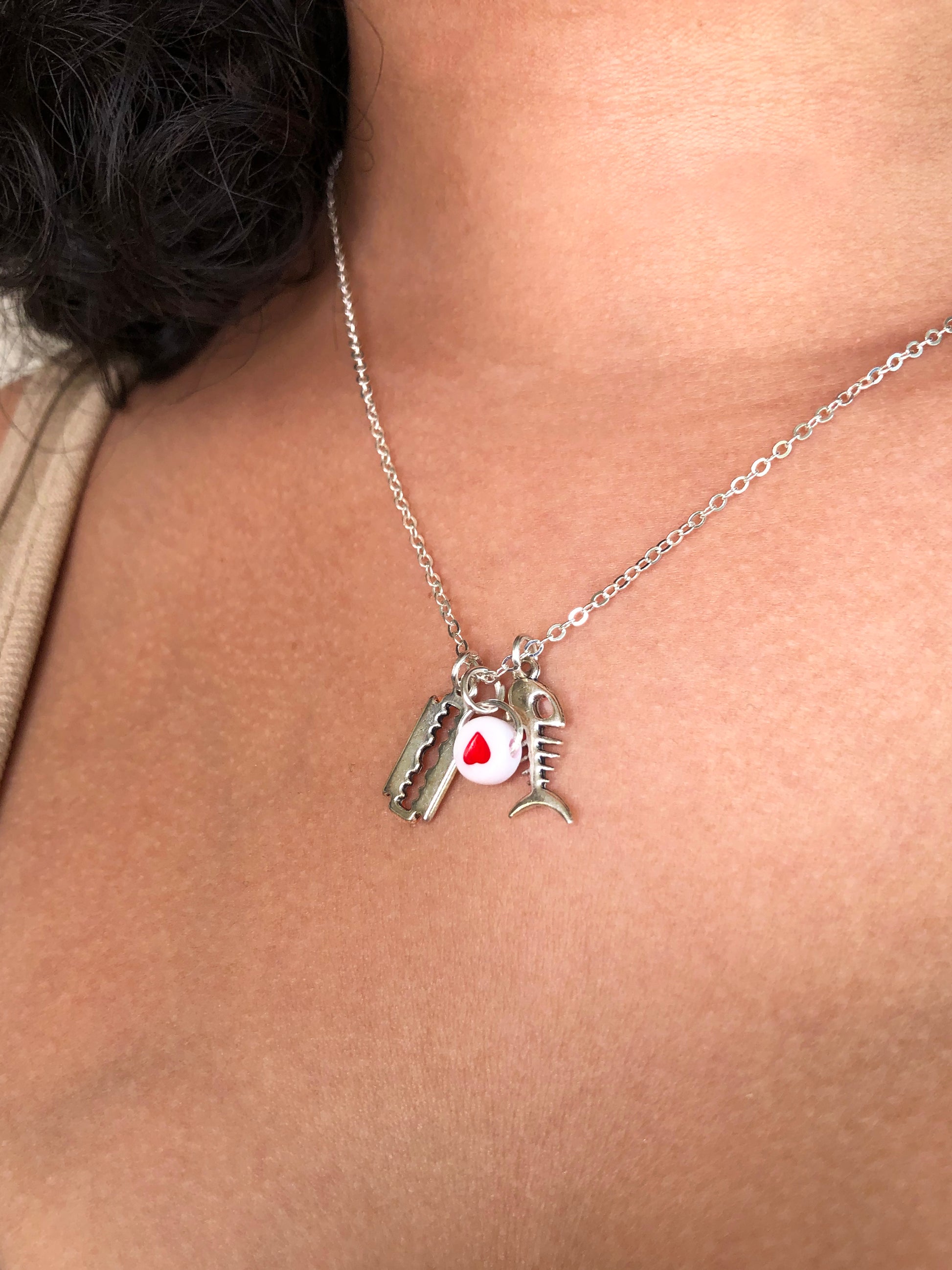 Handmade pendant necklace with a red flat round heart bead, a silver razor blade and skeleton fish charm.