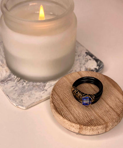 handcrafted ring made using a thick black wire wrapped base with a golden wire wrapped blue cube centerpiece.