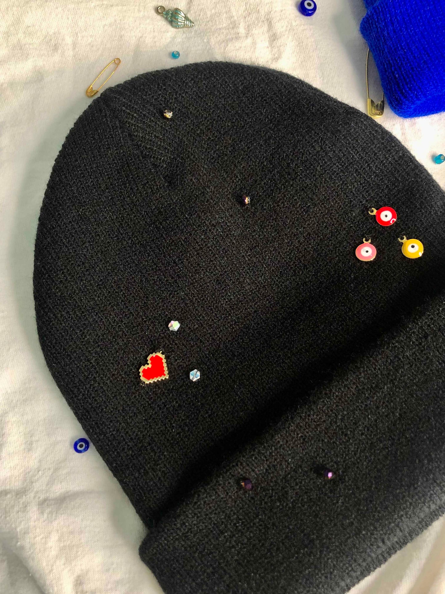 A black beanie accessorized using a heart charm, evil eye charms, and crystal beads. 