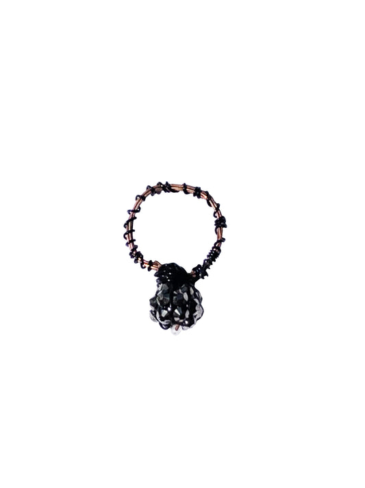 handcrafted intertwined rose gold and black wire wrapped ring with a silver and black charm, and a single clear bead at its center.