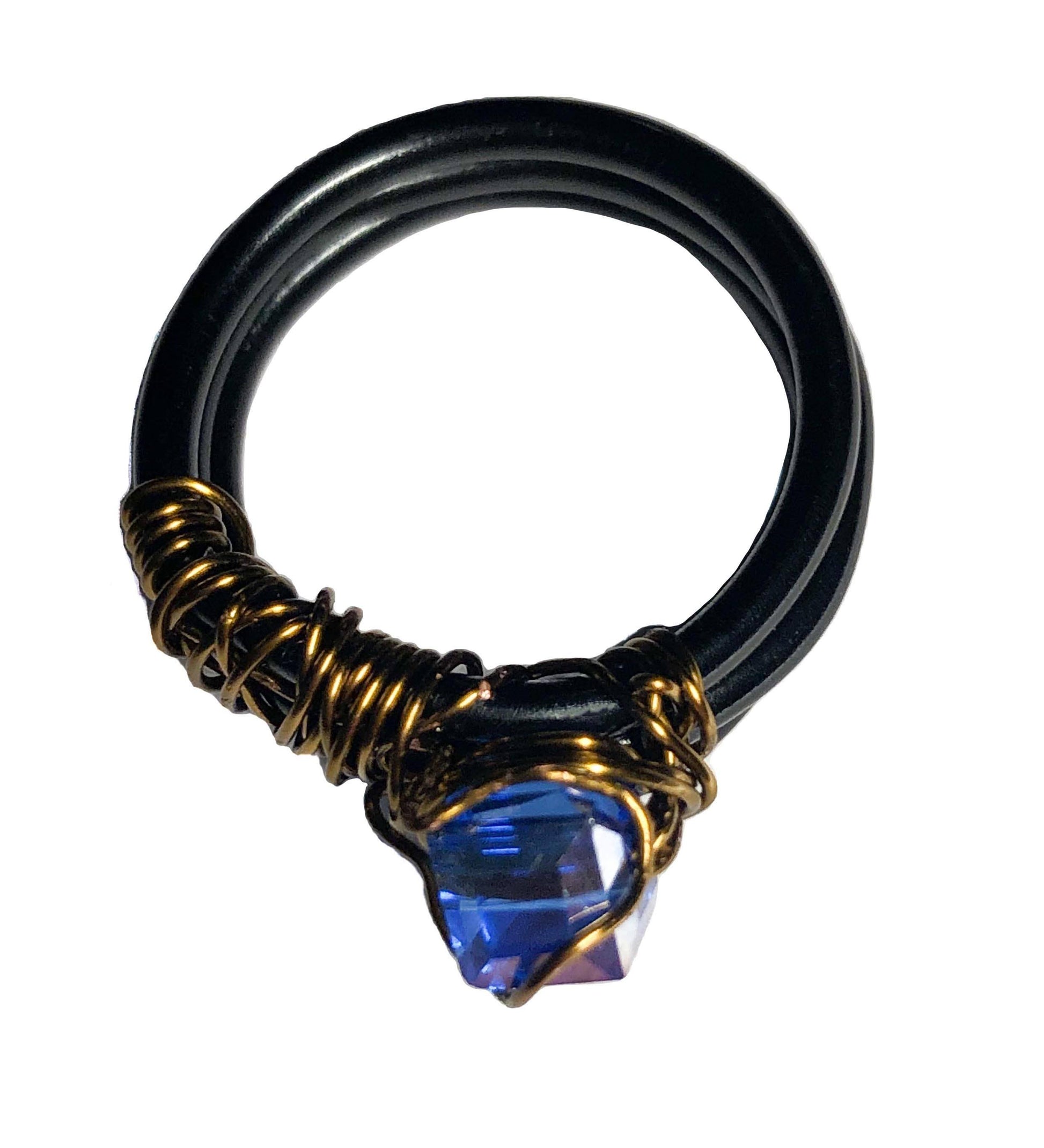 handcrafted ring made using a thick black wire wrapped base with a golden wire wrapped blue cube centerpiece.