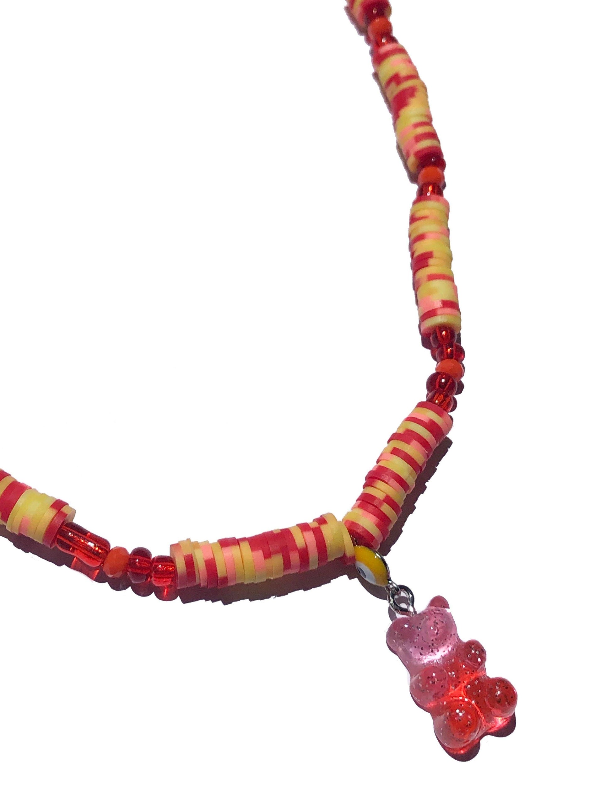 handcrafted necklace beaded using red, orange, yellow and pink glass and flat rubber beads. Accompanied by a yellow evil eye, and pink and orange gummy bear-like charm.